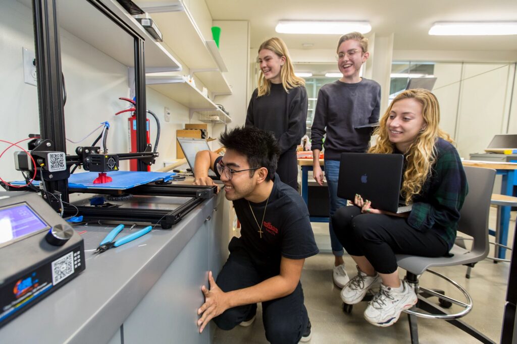 Students watch a 3D printer at work